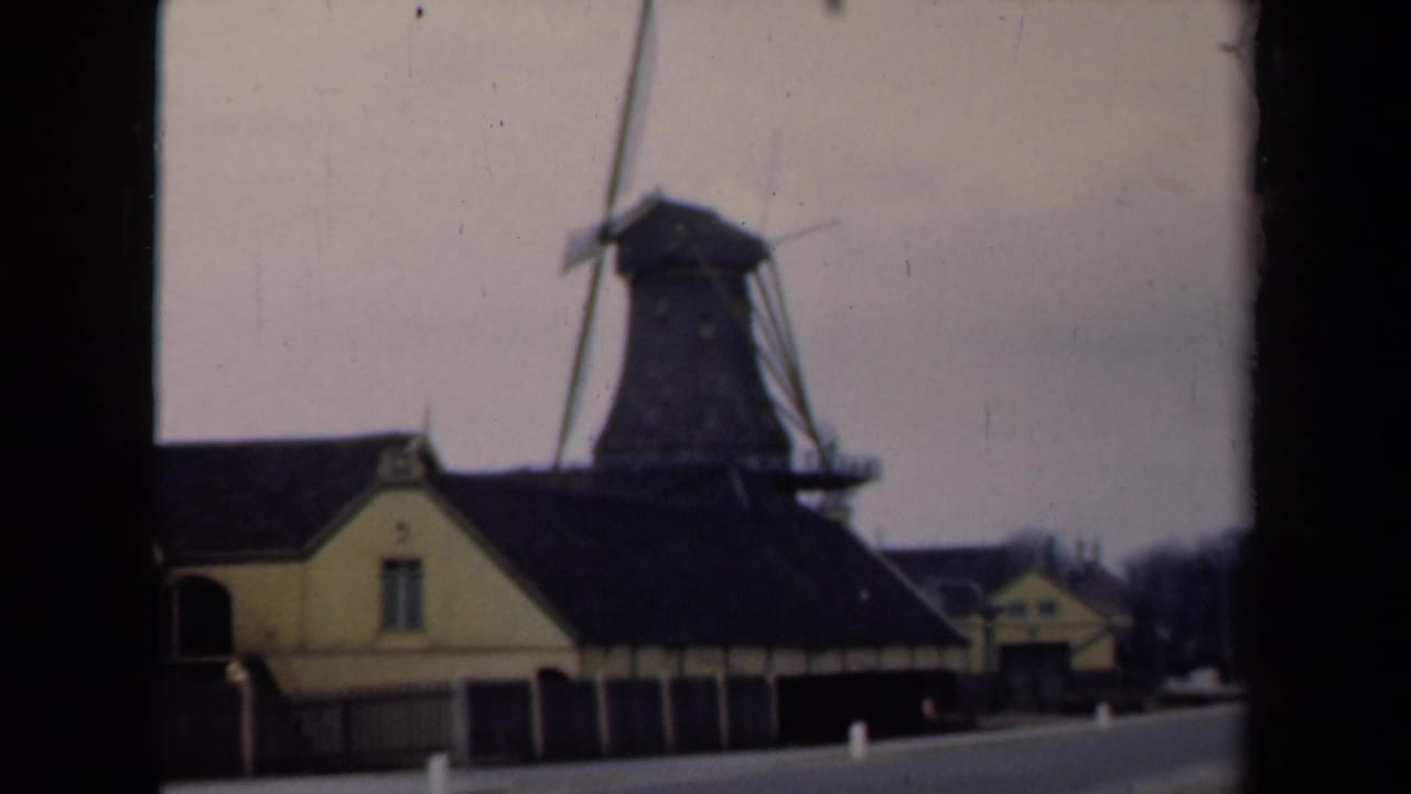 Dutch windmill beside yellow roadside buildings, seen through dark film frame edges.