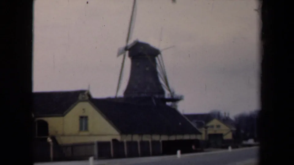 1946 Netherlands 8mm frame showing a traditional windmill and yellow buildings from a roadside viewpoint.