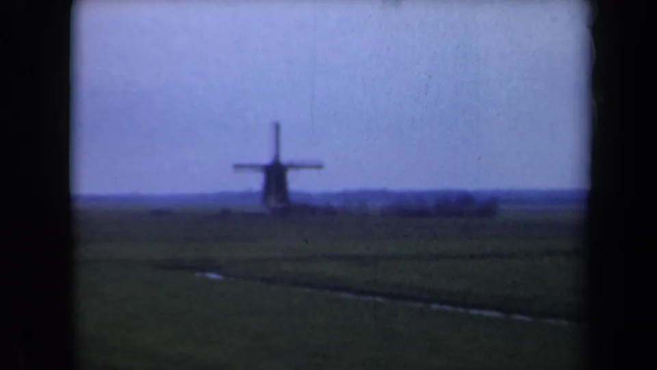 1946 Netherlands 8mm frame showing a distant windmill on the horizon beyond a flat green field and pale blue sky.