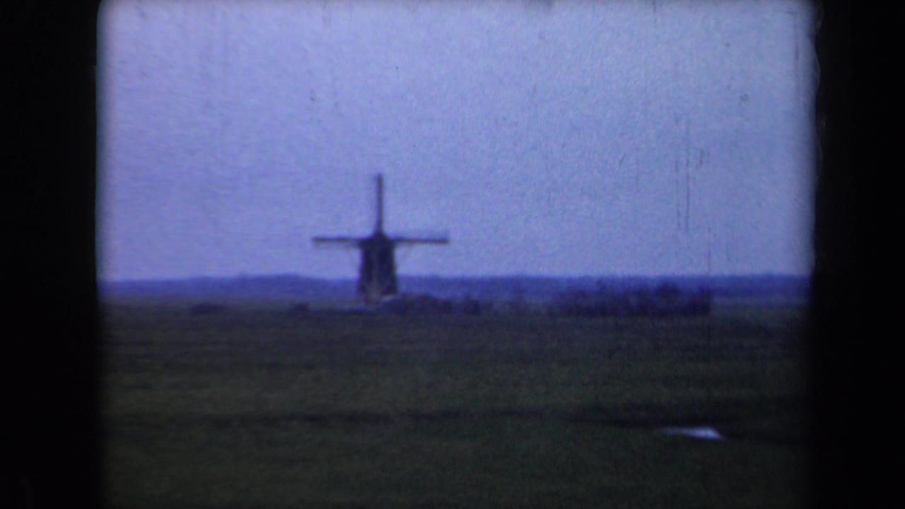 Windmill near the horizon with open field and dark film borders.