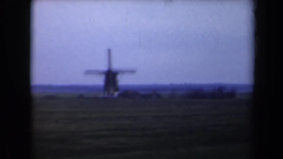 A distant windmill in the Netherlands appears across flat countryside in a blue-tinted 1946 8mm home-movie frame.