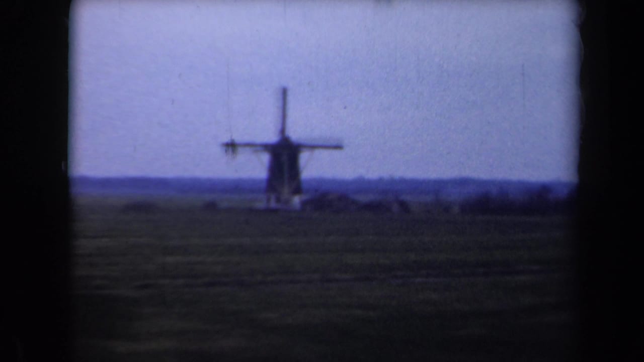 1946 Netherlands home-movie frame showing a distant windmill across flat fields beneath a fading evening sky.