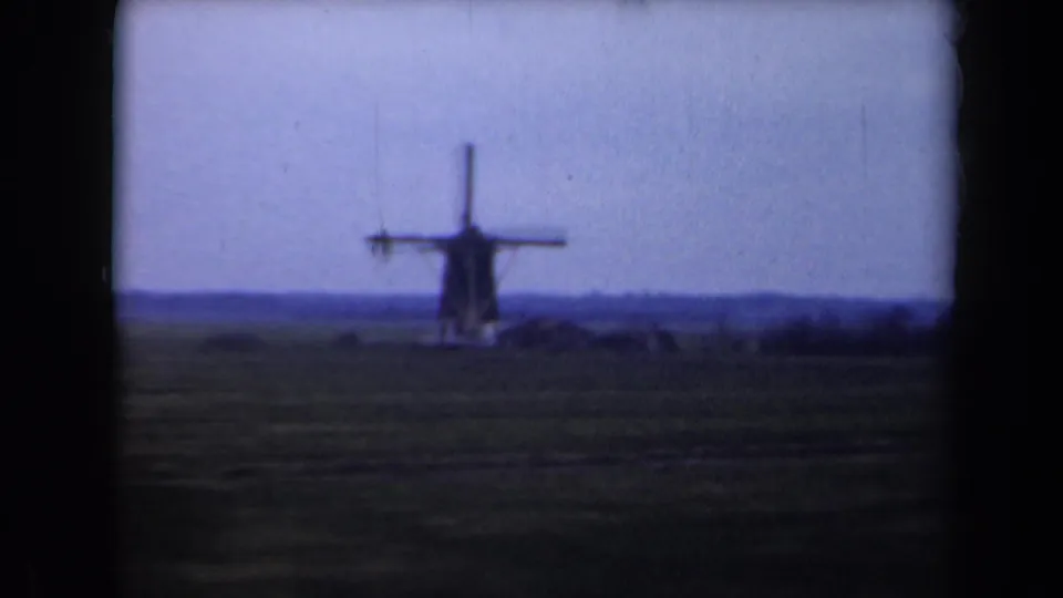 1946 Netherlands home-movie frame showing a distant windmill across flat fields beneath a fading evening sky.