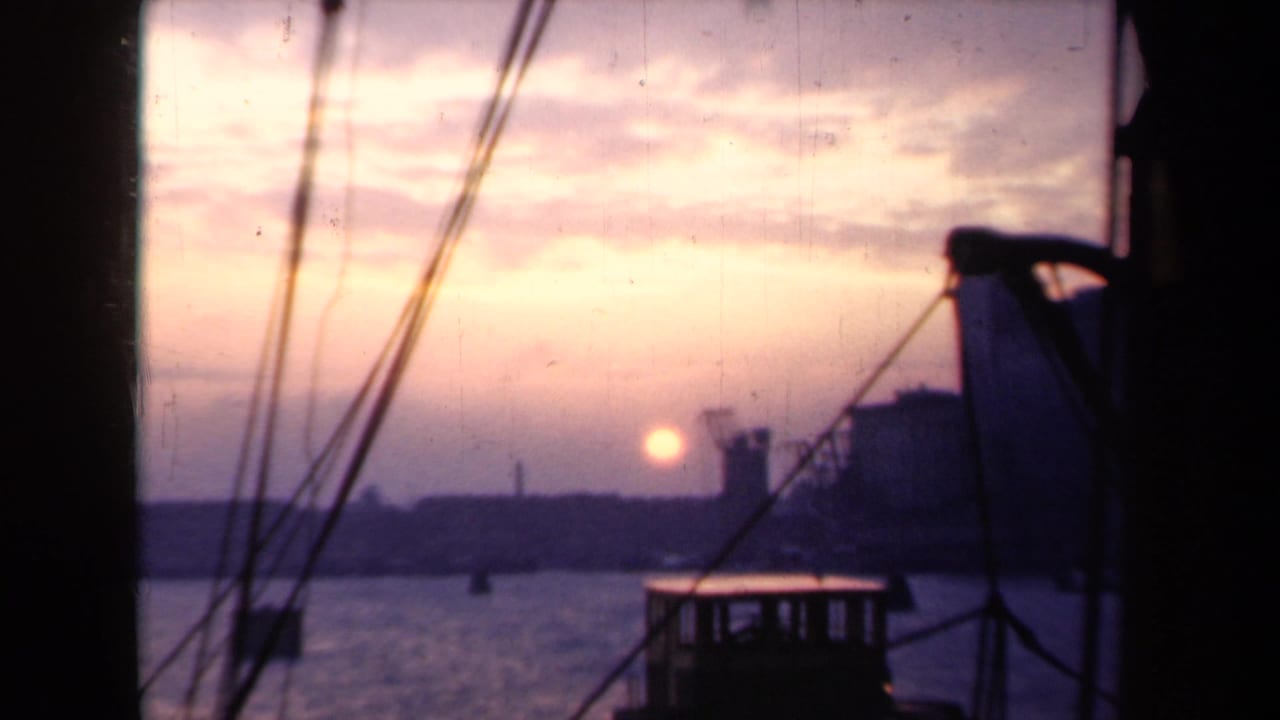 Harbor sunset seen past boat rigging and a dark deck structure.