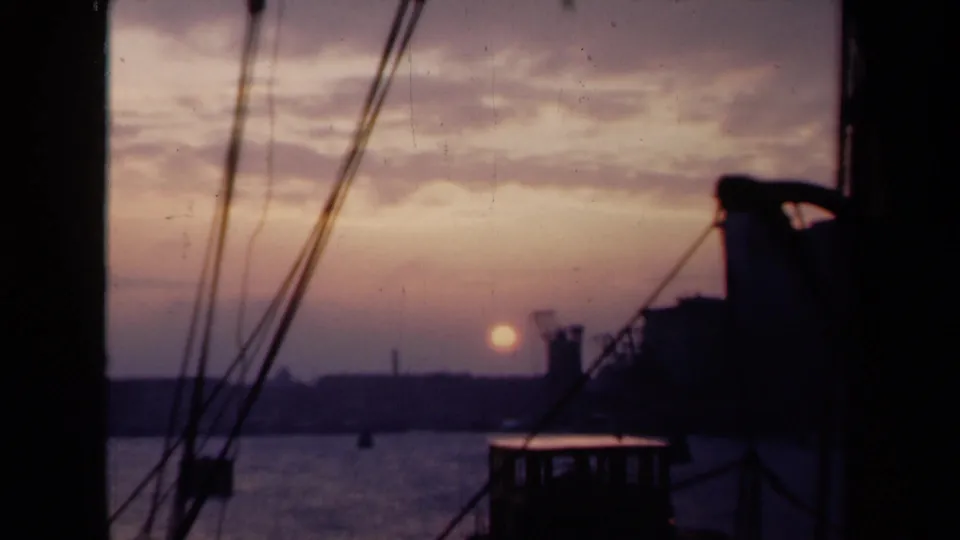 1946 Netherlands travel footage frame with the low sun over a harbor, seen through diagonal lines of boat rigging.
