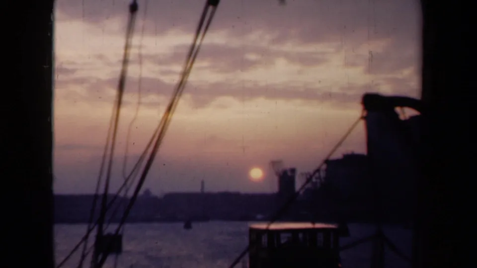 1946 Netherlands harbor sunset from a boat, showing the sun near the horizon with rigging and silhouetted waterfront forms.
