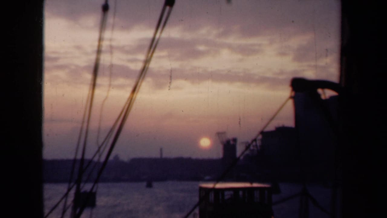 1946 Netherlands harbor sunset with calm water, dark rigging, a low shoreline, and industrial silhouettes in the distance.