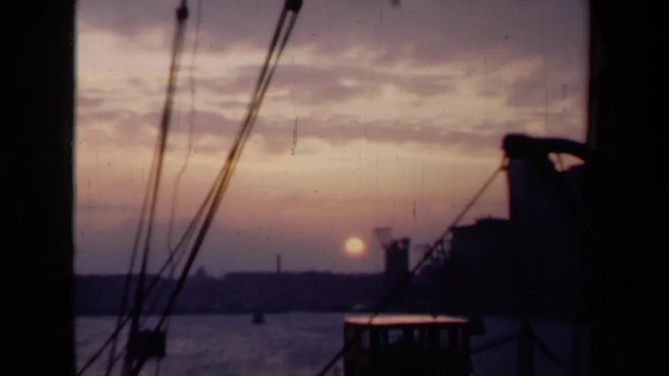 1946 Netherlands harbor sunset with calm water, dark rigging, a low shoreline, and industrial silhouettes in the distance.