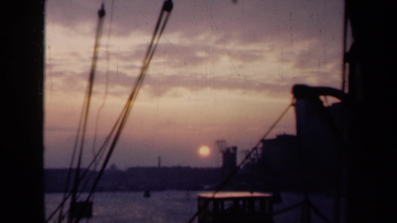 Harbor sunset with rigging in the foreground and dark waterfront shapes on the horizon.