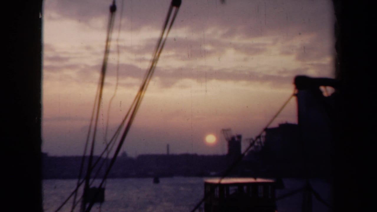 Archival 8mm Netherlands harbor sunset with foreground rigging, a dark vessel edge, calm water, and distant waterfront silhouettes.