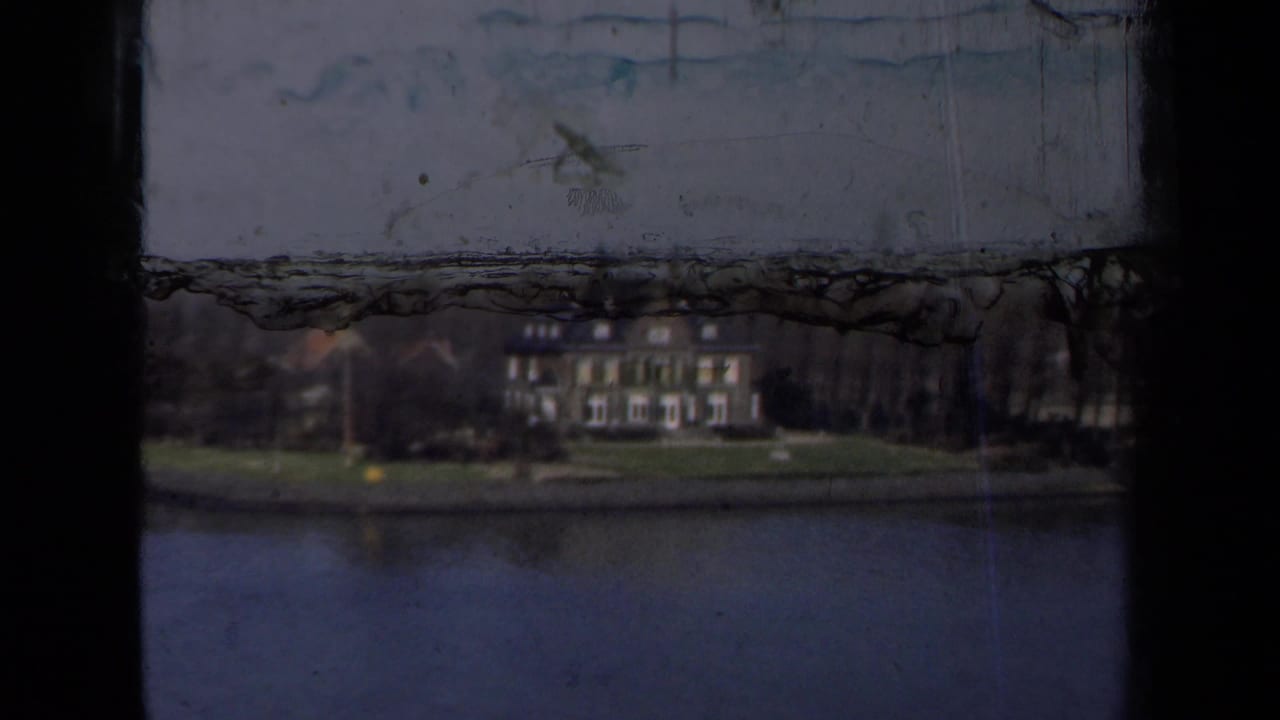 1946 Netherlands home-movie frame showing a large waterside house across calm water, partly obscured by dark film-frame edges.