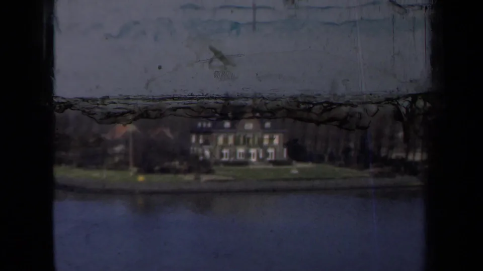 1946 Netherlands home-movie frame showing a large waterside house across calm water, partly obscured by dark film-frame edges.