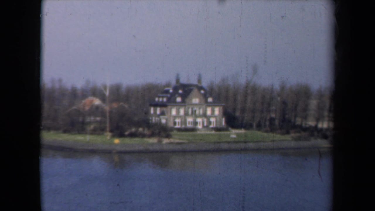 Large house on a grassy lakeshore seen from across calm water.
