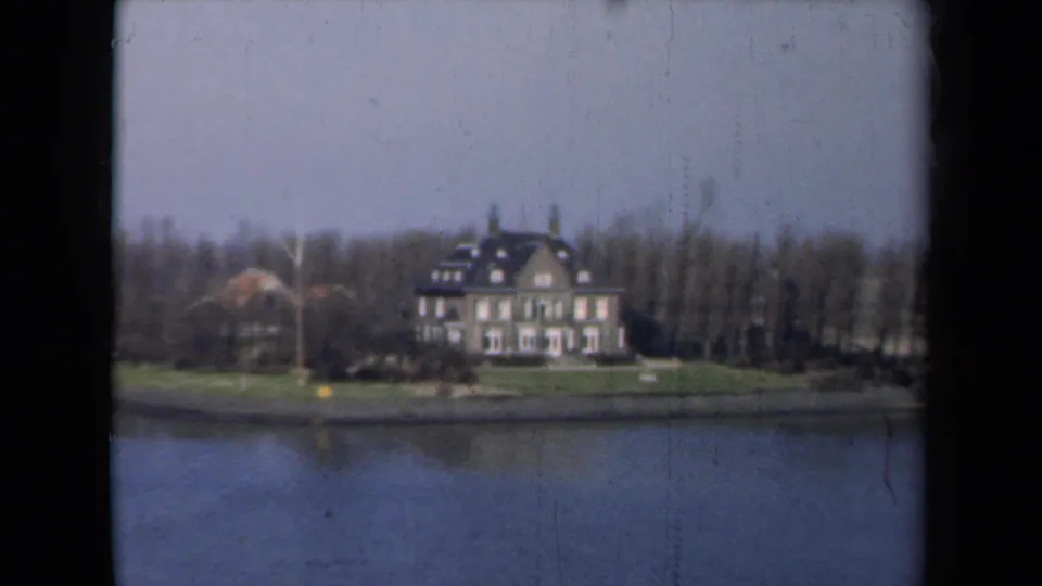 1946 Netherlands frame of a stately house on a grassy waterfront with bare trees and calm water in the foreground.