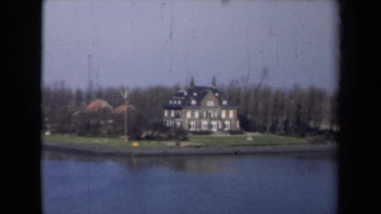 1946 Netherlands 8mm view of a large house beside water, with a lawn, bare trees, and soft home-movie color.
