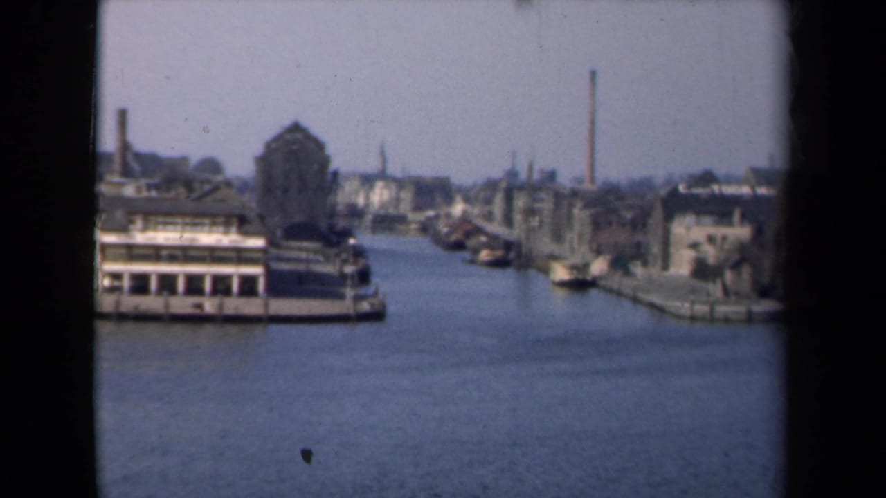 1946 Netherlands 8mm frame with a foreground canal boat, older waterfront structures, and distant chimneys along the waterway.