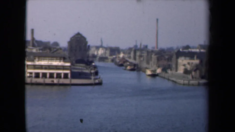 1946 Netherlands 8mm frame with a foreground canal boat, older waterfront structures, and distant chimneys along the waterway.