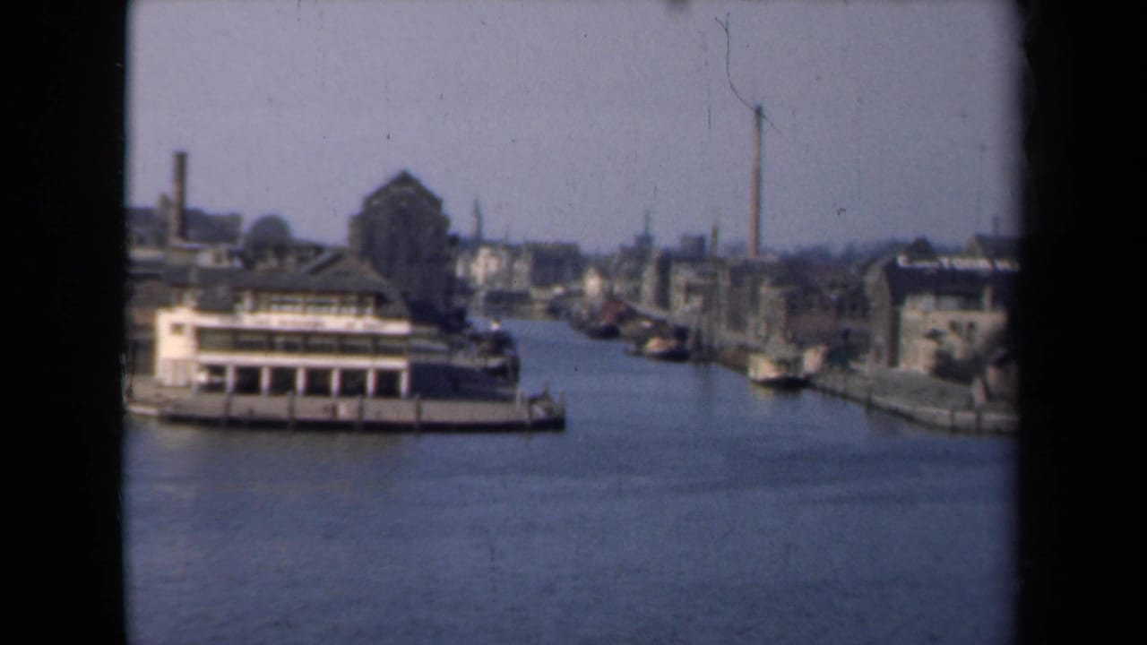 1946 Netherlands canal scene showing a large boat in the foreground, docked vessels, waterfront buildings, and a tall chimney beyond.