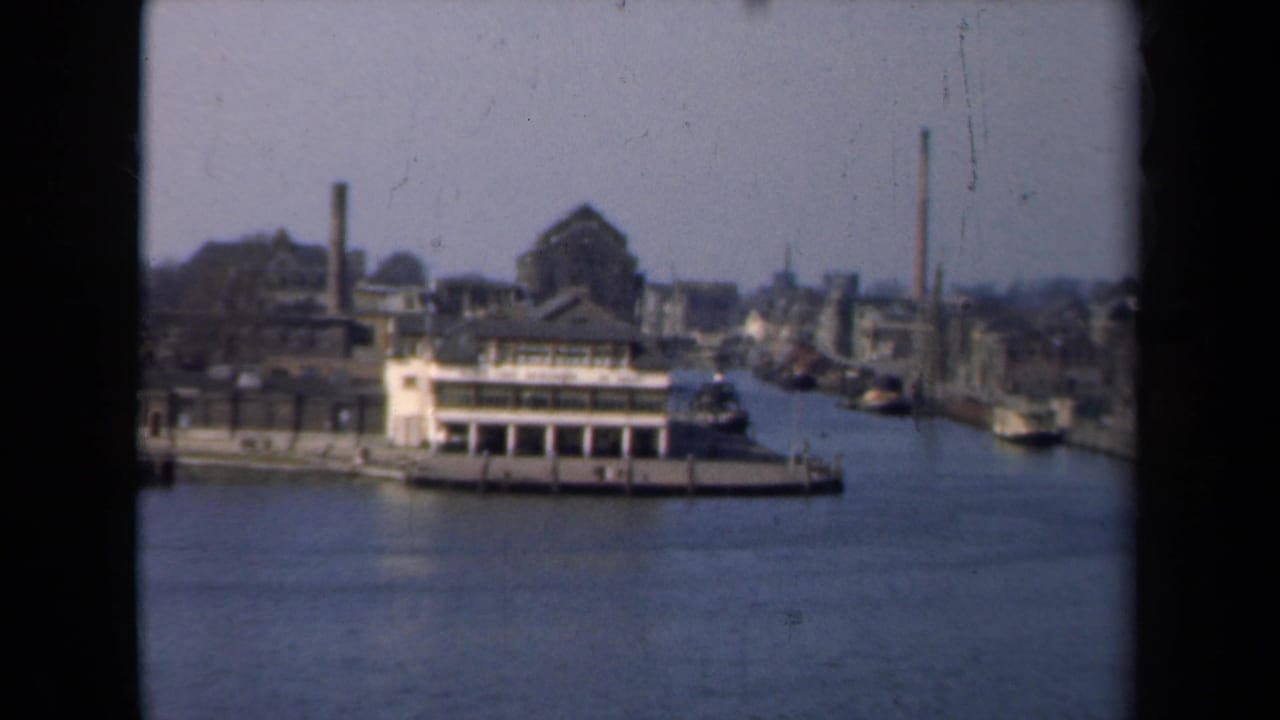 Similar canal view with a moored riverboat, waterfront buildings, and distant smokestacks.