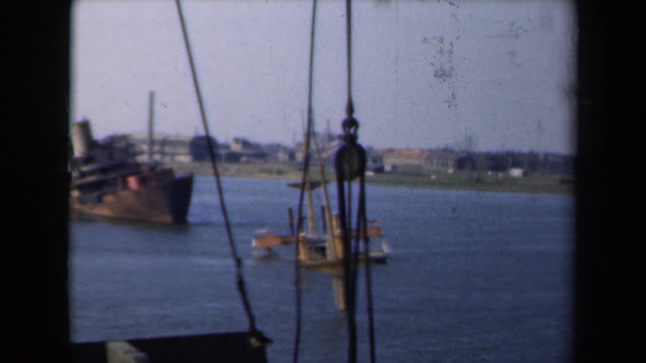 1946 Netherlands 8mm frame showing a damaged ship in a waterway, viewed from another vessel through rigging and pulley hardware.