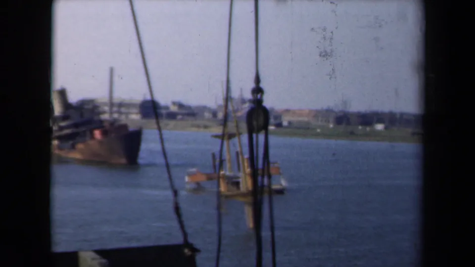 1946 Netherlands 8mm frame showing a damaged ship in a waterway, viewed from another vessel through rigging and pulley hardware.