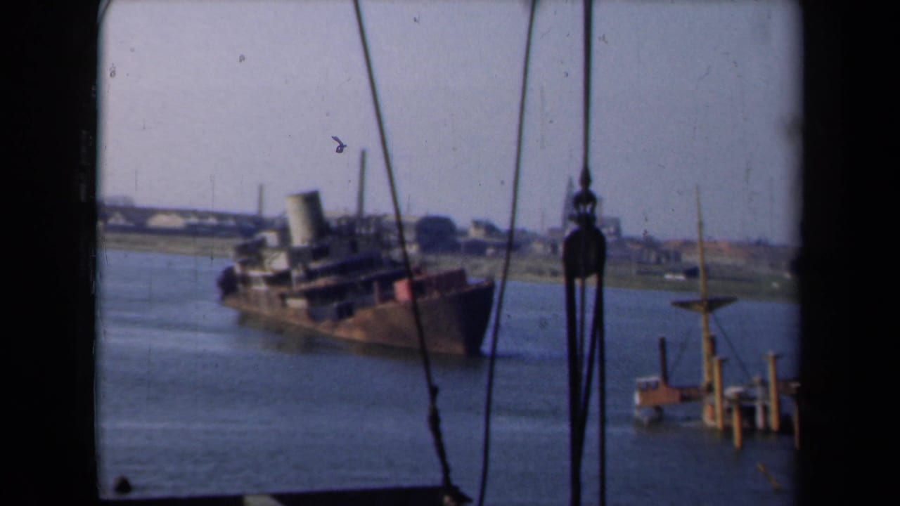 1946 Netherlands 8mm frame showing an old listing transport steamer in a shallow waterway, viewed through rigging or window framing.