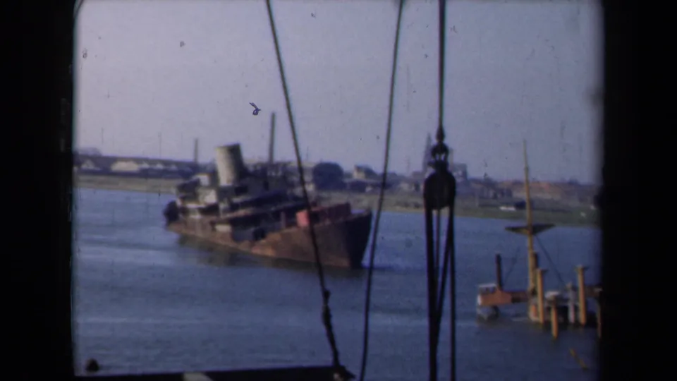 1946 Netherlands 8mm frame showing an old listing transport steamer in a shallow waterway, viewed through rigging or window framing.