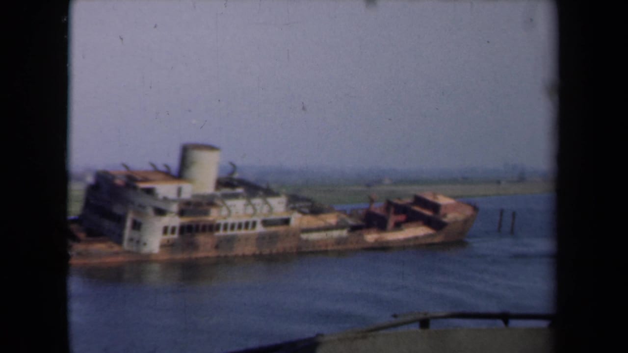 1946 Netherlands 8mm frame of the stranded transport steamer, its pale funnel and rusted listing hull visible on a shallow waterway.