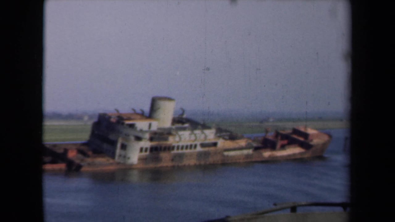 1946 Netherlands 8mm frame showing a rusted sunken vessel with white superstructure and smokestack above calm canal water.