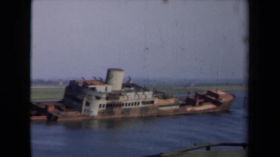 1946 Netherlands 8mm frame showing a rusted sunken vessel with white superstructure and smokestack above calm canal water.