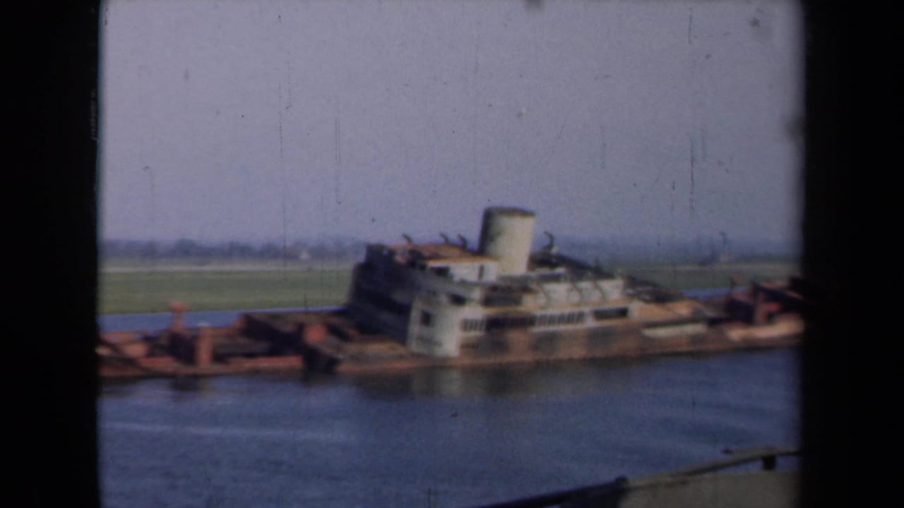 Sunken ship viewed from across calm water, framed by 8mm film borders.