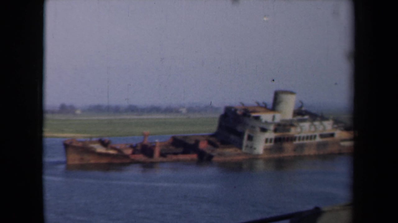 A closer 8mm view of the partially submerged vessel shows the corroded bow, white cabins, smokestack, and quiet Dutch canal setting.