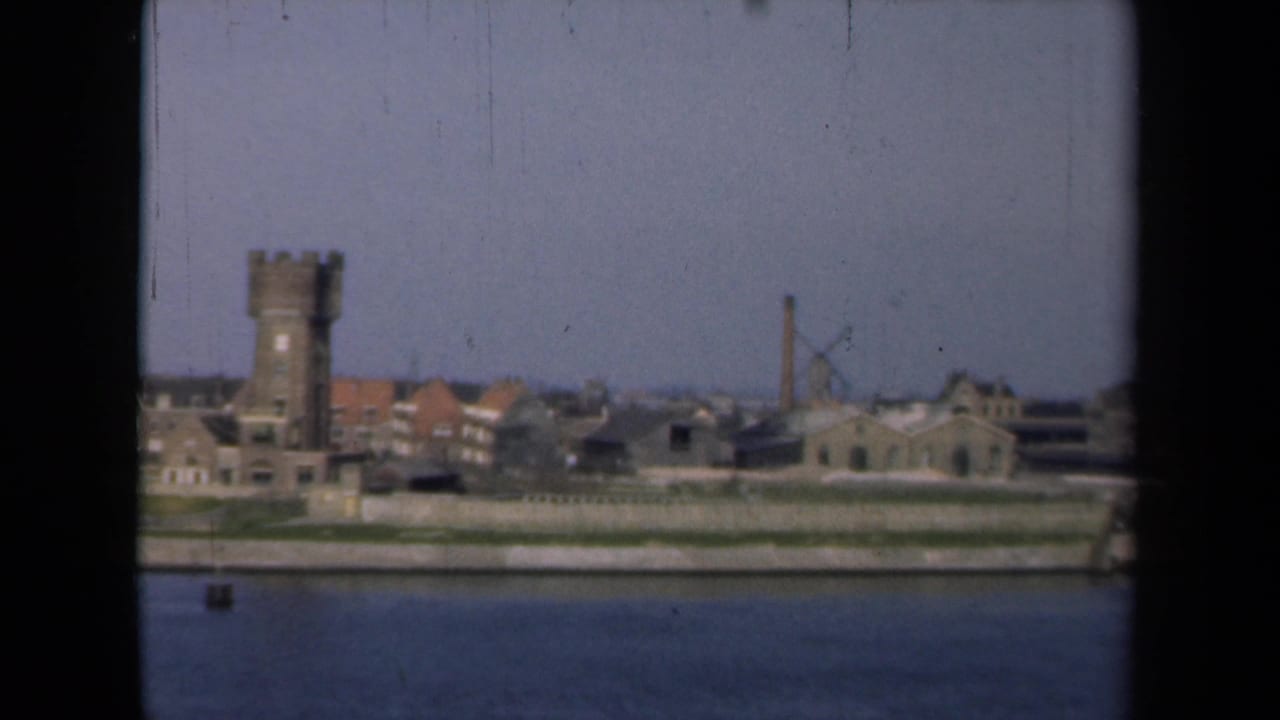 Waterfront with tower, Dutch-style buildings, windmill, chimney, and river foreground.