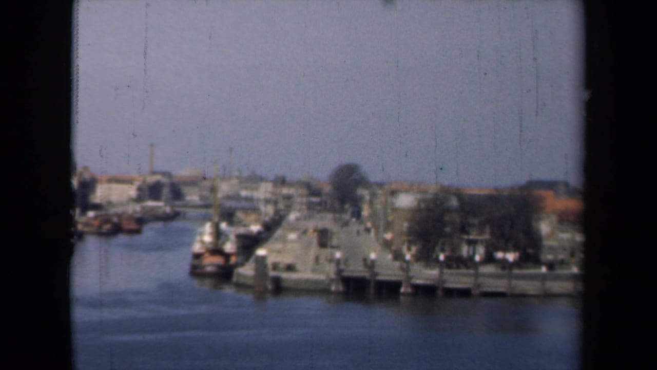 1946 Netherlands canal-town view from a boat, showing water, small moored boats, piers, and low waterfront buildings.
