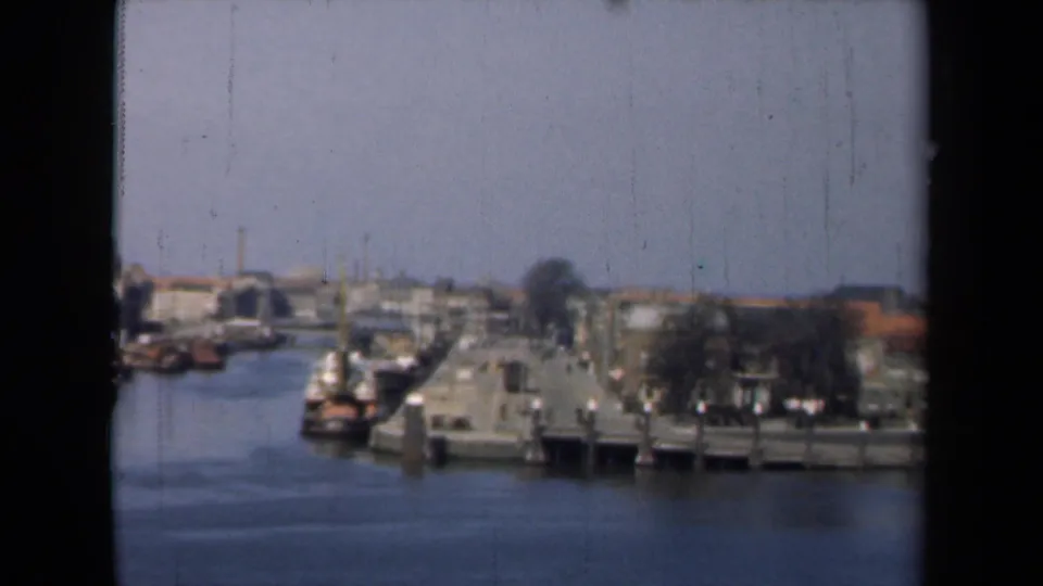 1946 Netherlands canal-town view from a boat, showing water, small moored boats, piers, and low waterfront buildings.