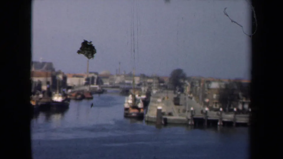 1946 Netherlands canal scene with small boats, a quayside, low buildings, a lone tree, and distant waterfront structures.