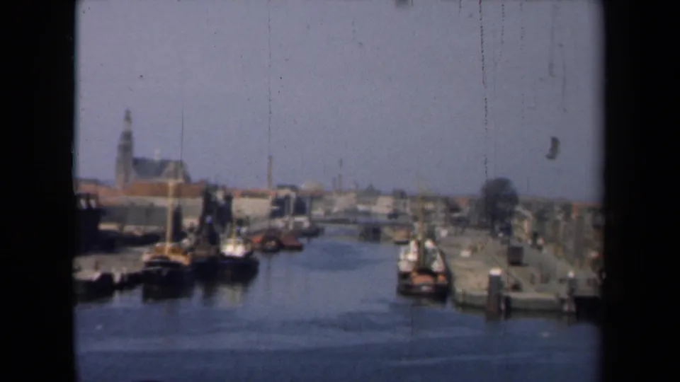 1946 Netherlands canal-town view showing moored boats, waterfront roofs, piers, and a distant church steeple above the skyline.