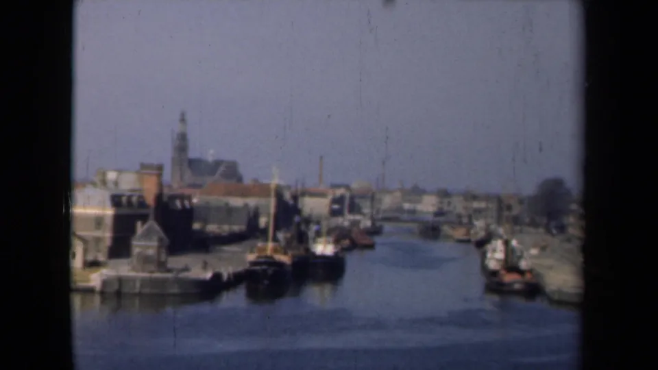 1946 Netherlands canal footage with boats near waterfront buildings, a quayside, piers, and a distant church steeple.