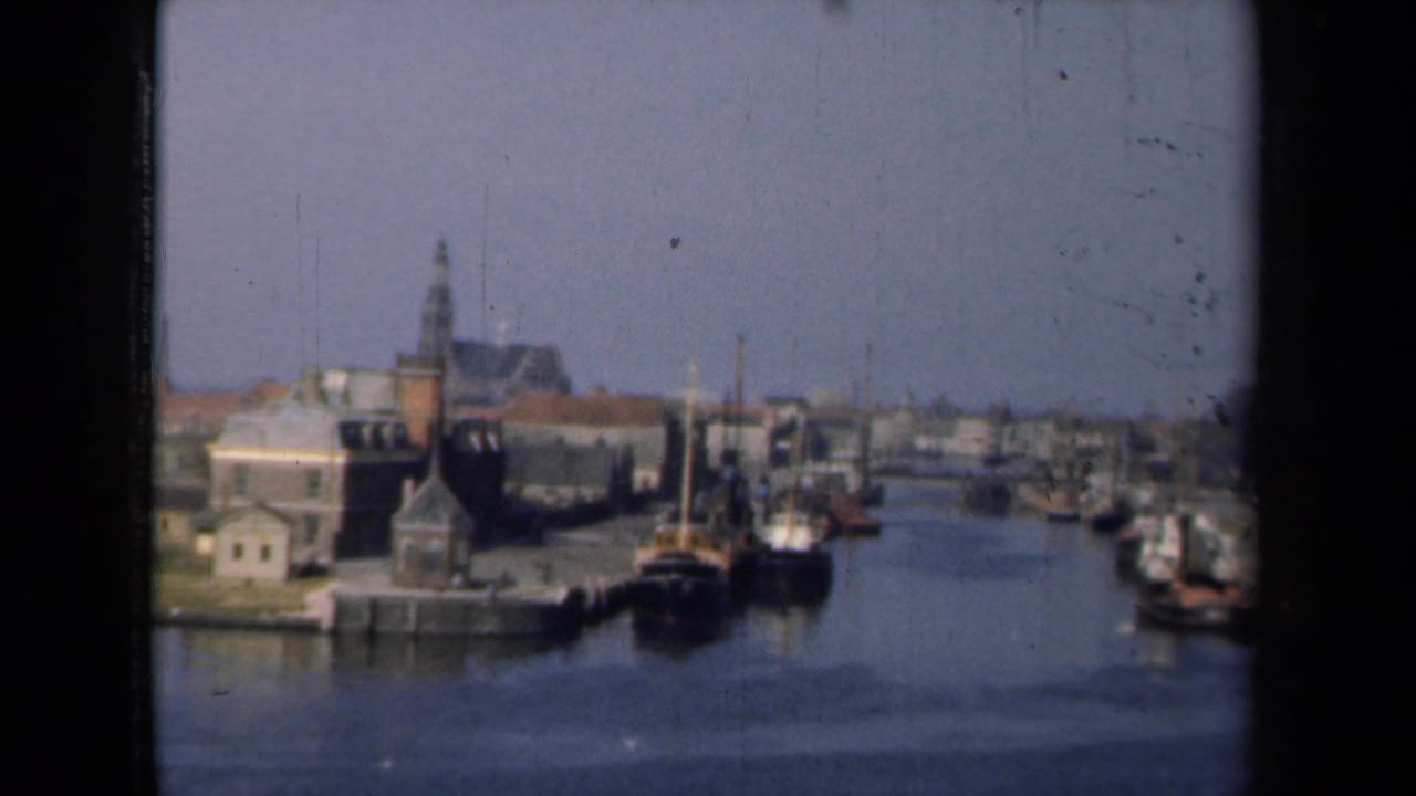Dutch harbor canal with moored boats, brick buildings, and a church steeple in the distance.