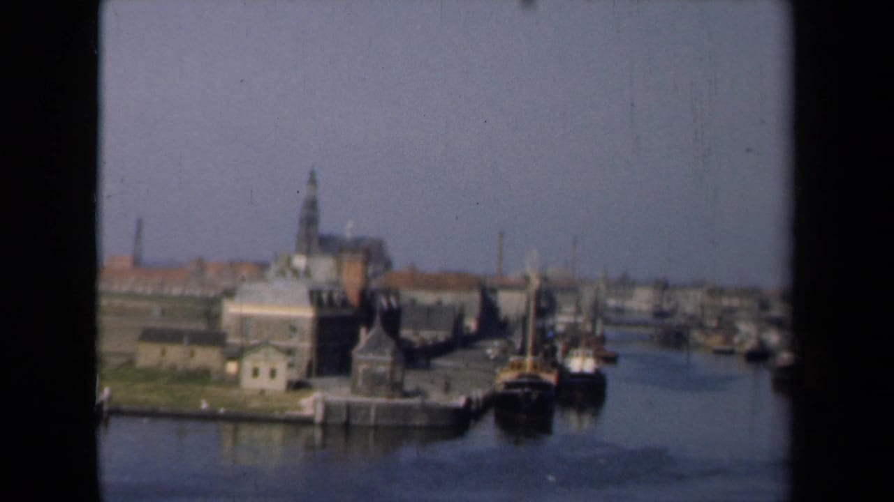 Harbor canal with boats near a pier and a church steeple rising above town rooftops.