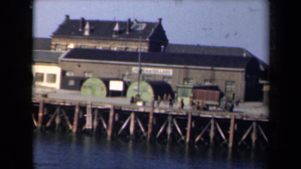 1946 Netherlands dockside view with an industrial building, green tanks, a military-style truck, and small figures on a timber pier.