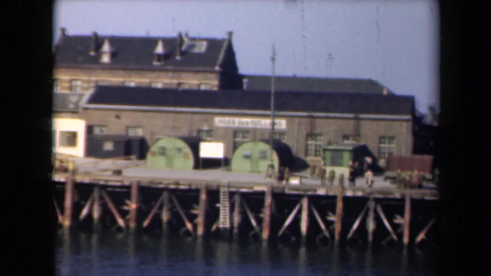 Final 1946 Netherlands dockside frame with timber pier, green tanks, military-style truck, people, and industrial signage visible.