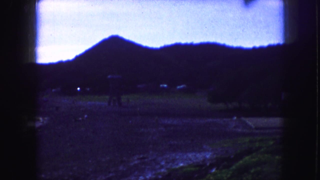 Dark hillside above a creek or wet ground, with blue sky and film gate edges.