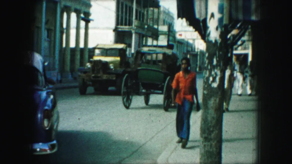 Kansas City street view with a carriage, early truck, blue car, pedestrians, and a woman walking near a street tree.