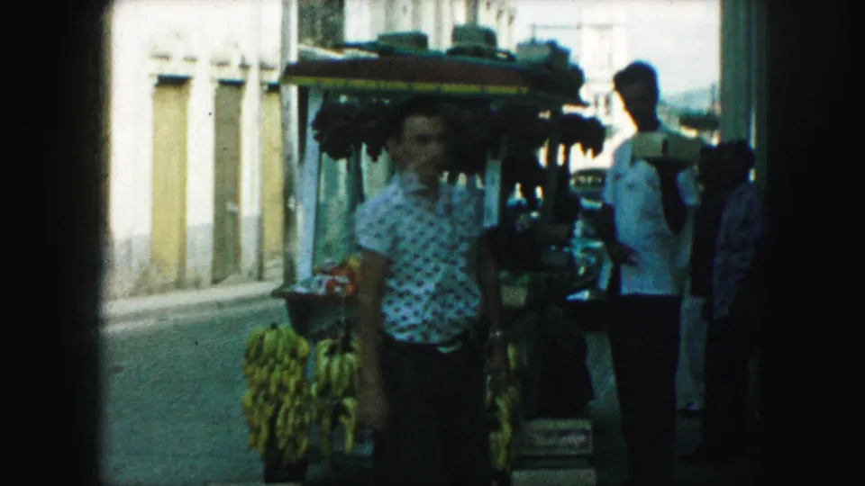 Sidewalk fruit stand in Kansas City with bananas and other produce as pedestrians stand and pass nearby.