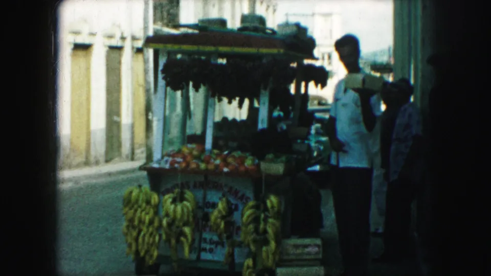 Kansas City sidewalk fruit cart with hanging bananas, produce boxes, and pedestrians gathered near the stand.