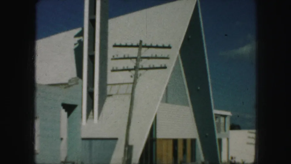 1959 Kansas City frame concentrating on the triangular modern building exterior, overhead lines, sidewalk, and clear sky.