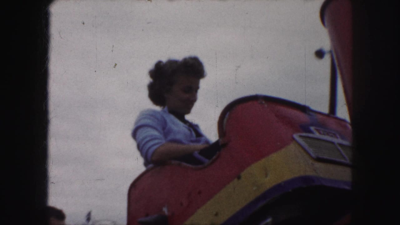 Young woman seated in a colorful roller coaster car under a cloudy sky.