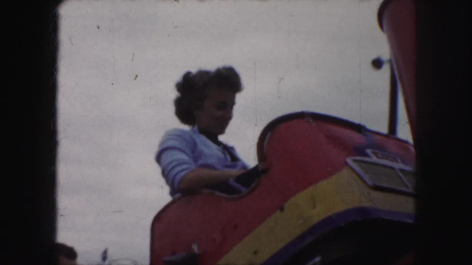 Young woman in a light sweater rides a red and yellow coaster car at Parque Colon in 1959 Kansas City footage.