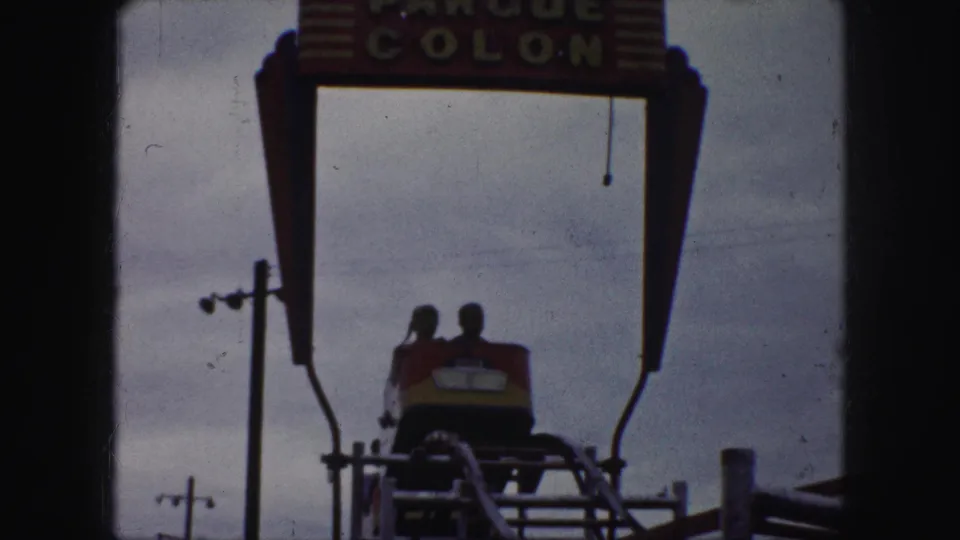 Riders in a red and yellow coaster car appear beneath the Parque Colon sign in Kansas City home-movie footage.